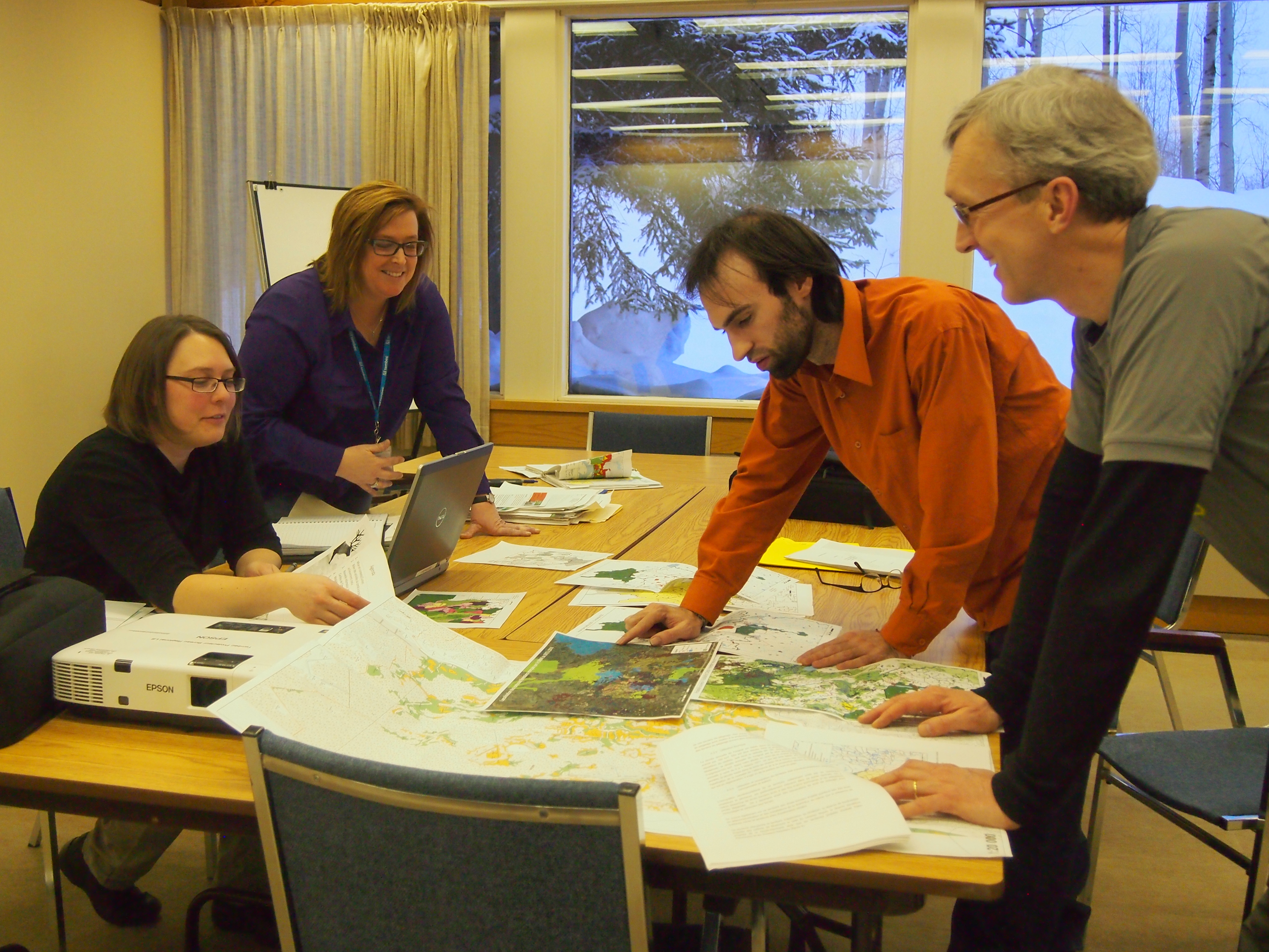 A group of four people gathered around a table filled with maps and papers