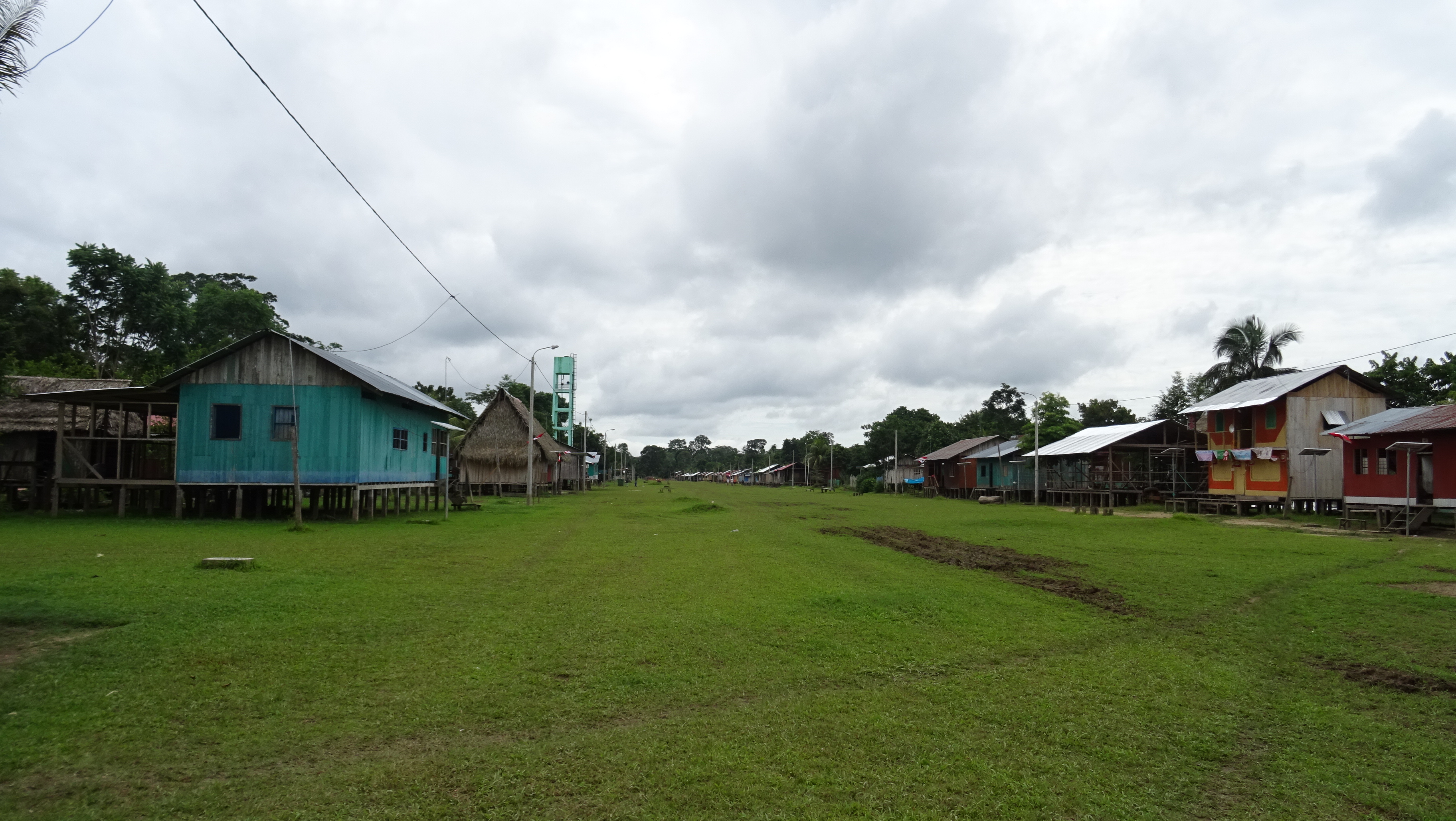 Indigenous community in the Amazon, buildings on either side of green grass, cloudy sky