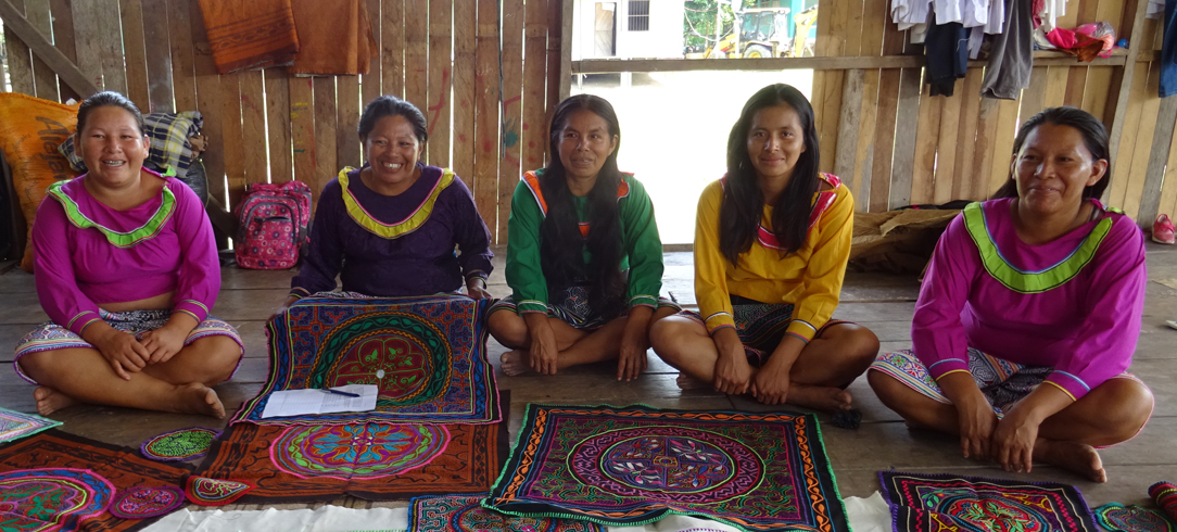 Calleria women sit smiling in front of their handwoven textiles