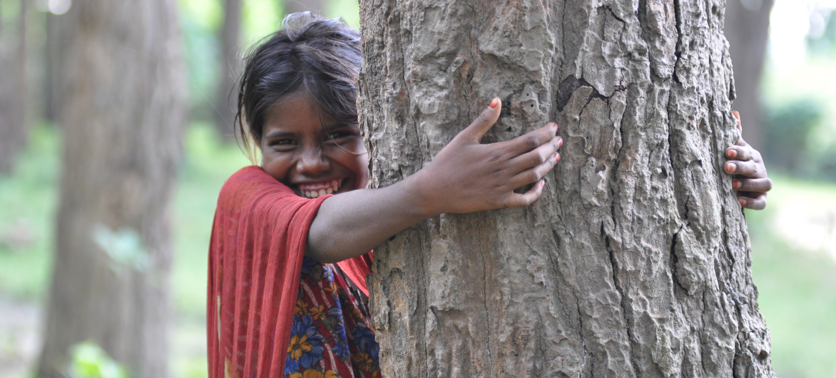 little girl hugs tree trunk and smiles