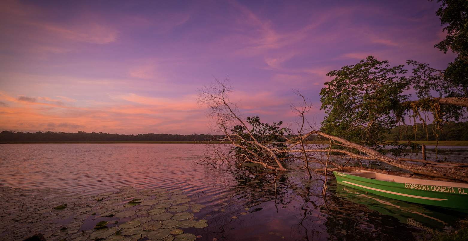 pink orange and purple sunset on a lake with a small boat and lilly pads in the foreground