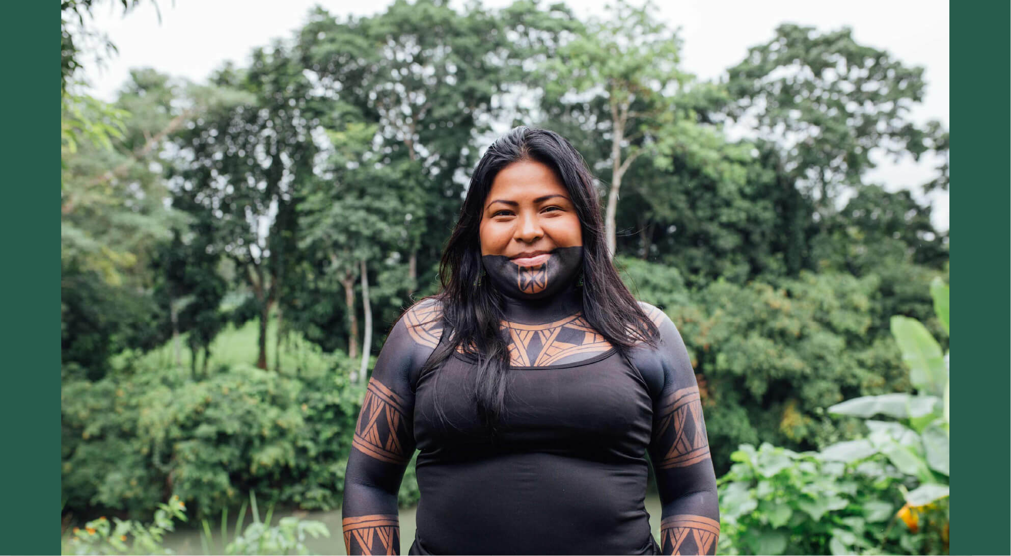 An Indigenous woman smiles softly at the camera while standing in a tropical forest setting.