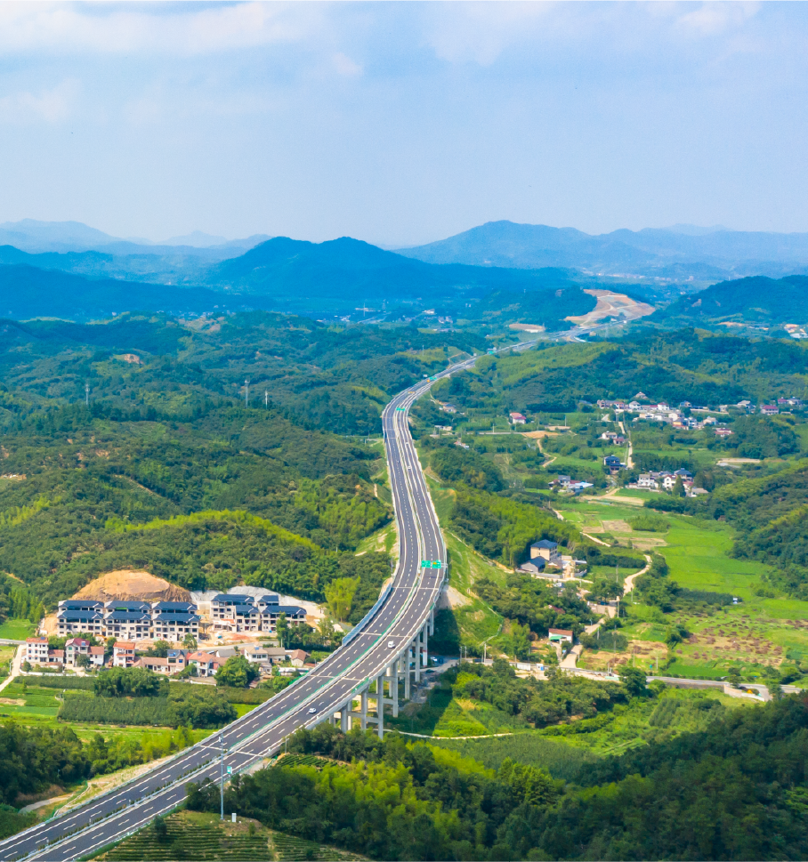 Skyview of a long highway road surrounded by forested areas with clusters of buildings.