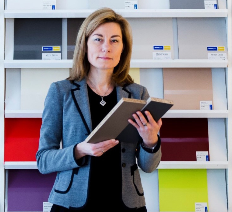 Natalia Pokinska holding notebooks in front of paper shelf