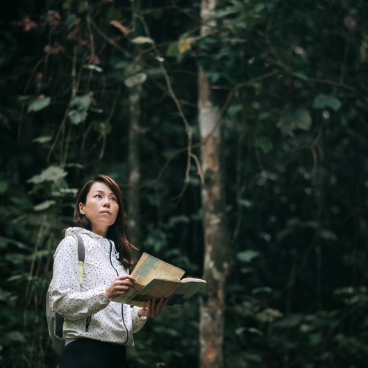 Woman holding a map in a dark green forest 
