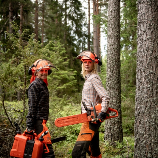 Woman standing in a forest with a hard hat and chainsaw