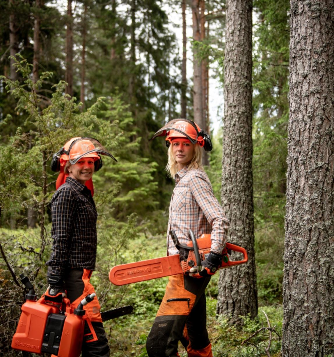 Two women standing in a forest with hardhats and chainsaws