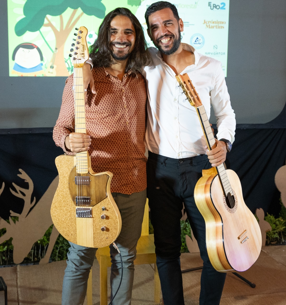 two men each holding a guitar smiling together for a picture
