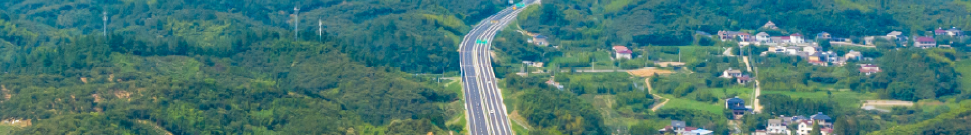 Skyview of a long highway road surrounded by forested areas with clusters of buildings.