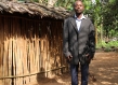 Man in Congo wearing suit jacket stands for portrait in front of hut