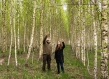 A man and woman look up and point at a collection of trees while standing in the forest.