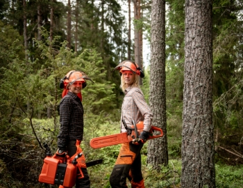 Two women standing in a forest with chainsaws and hardhats