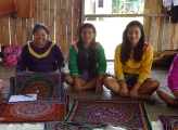 Calleria women sit smiling in front of their handwoven textiles