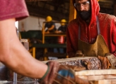 Photo of two men cutting wood planks with a bandsaw.