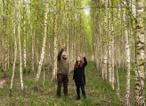 A man and woman look up and point at a collection of trees while standing in the forest.